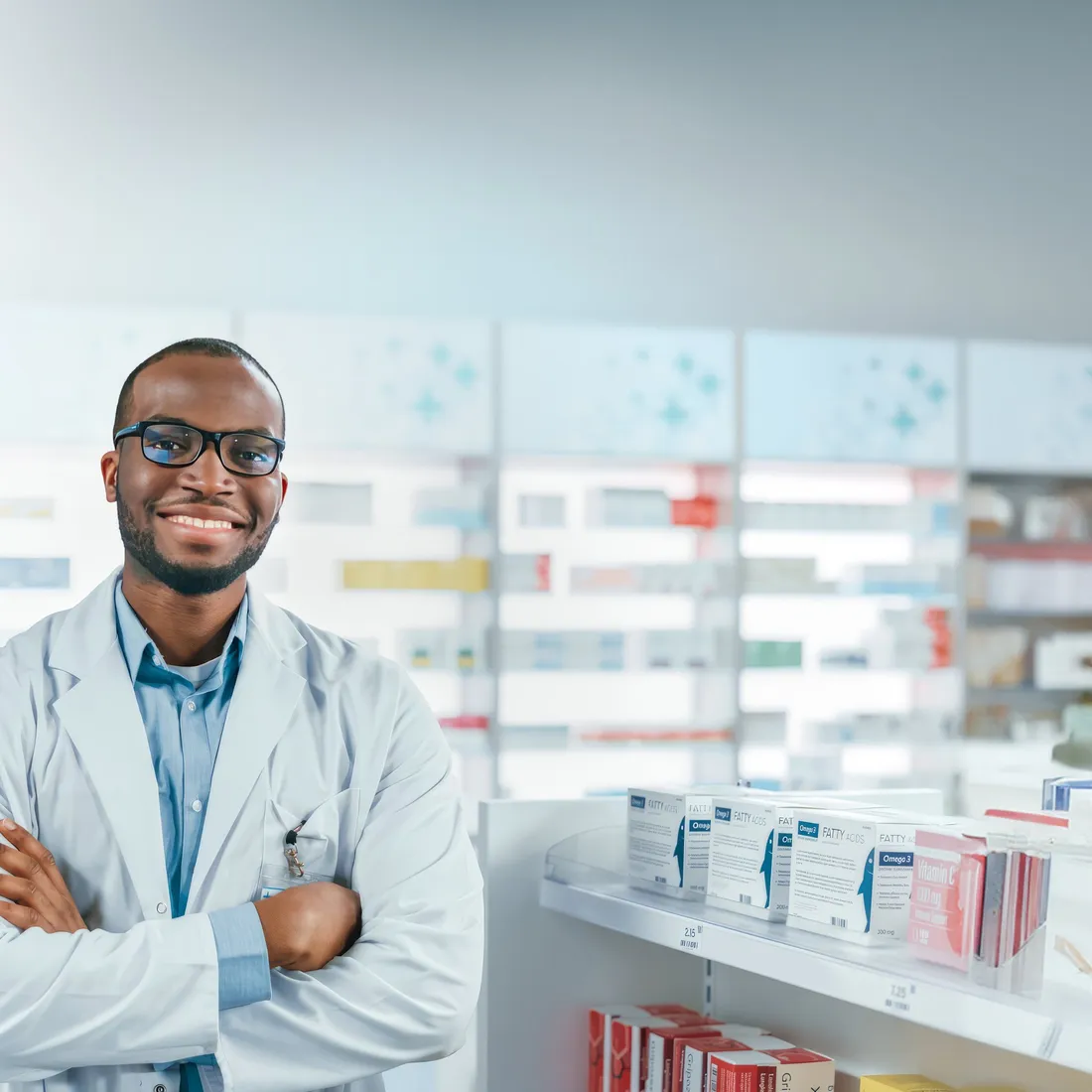 A smiling pharmacist with his arms crossed in front of pharmacy shelves