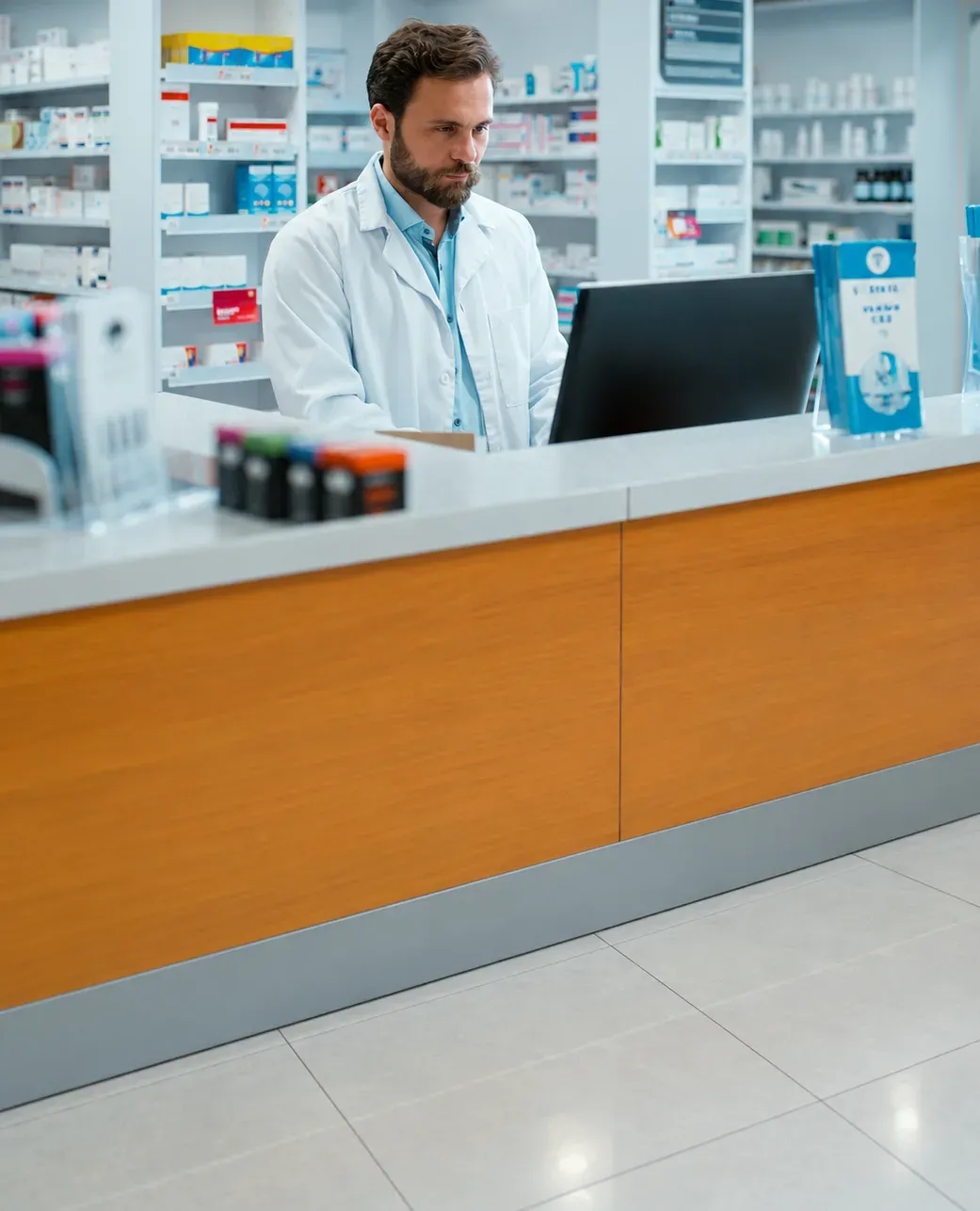 A pharmacist working at a computer behind the pharmacy counter